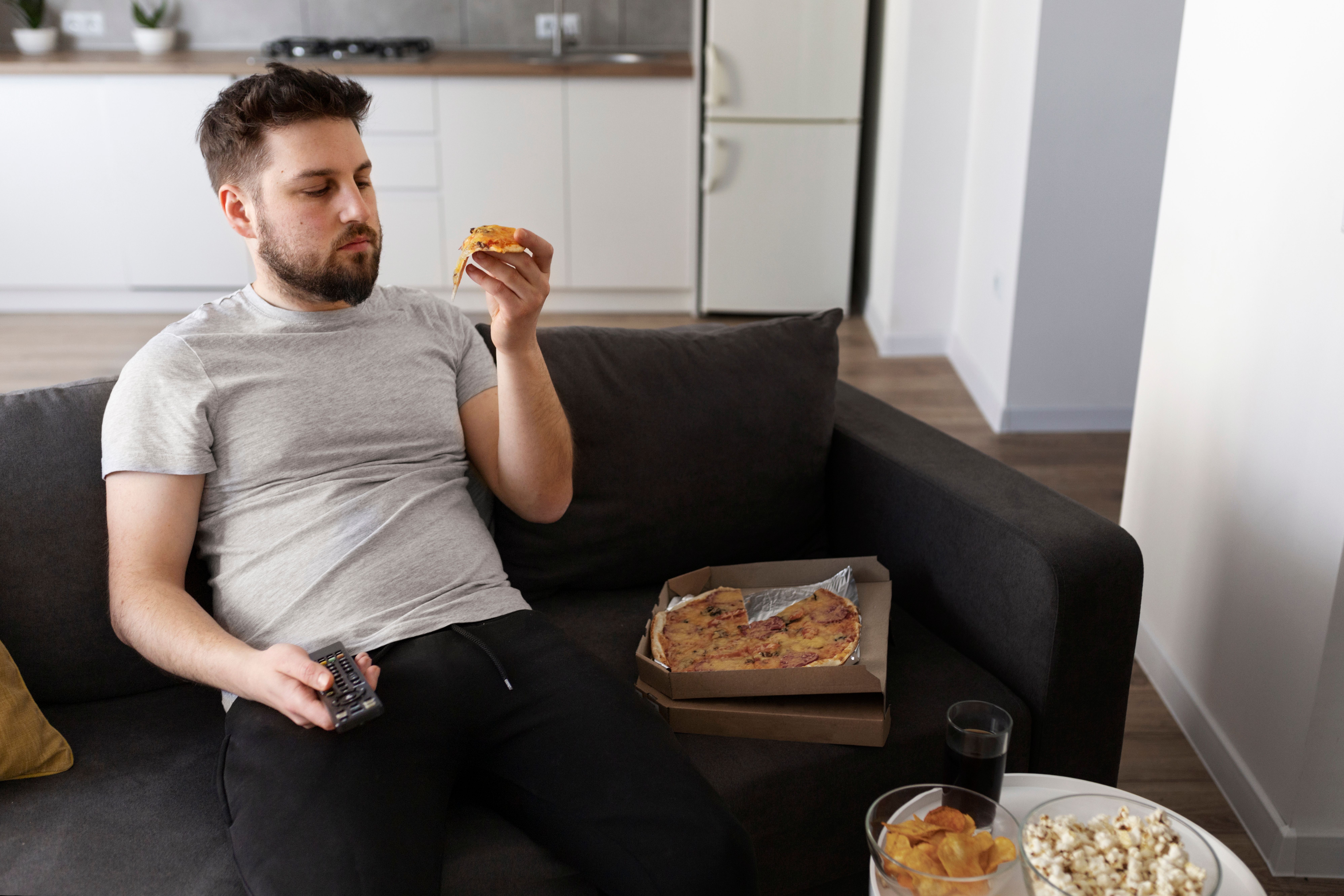 Man eating pizza while watching TV on couch.