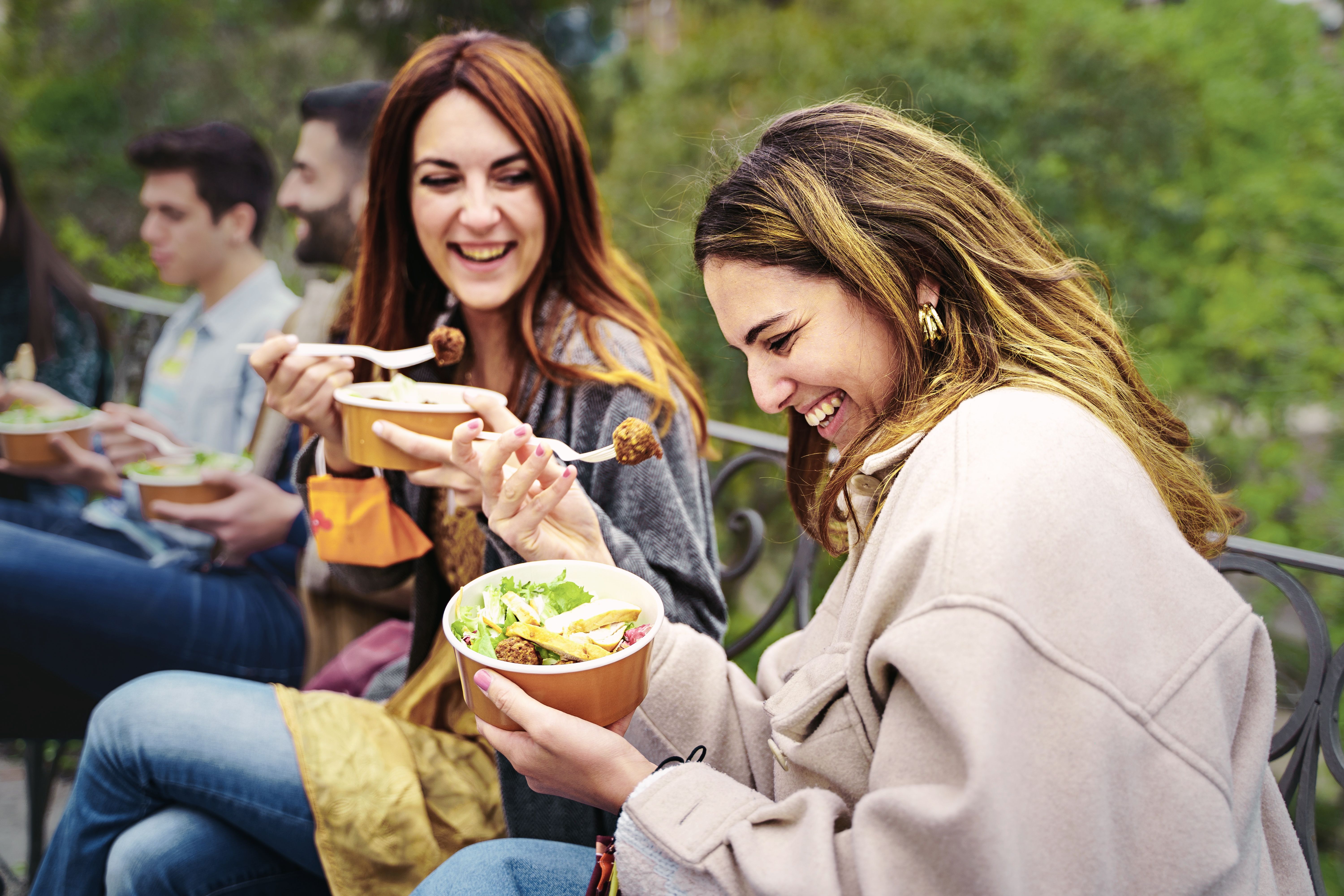 Friends laughing while enjoying a meal outdoors together.