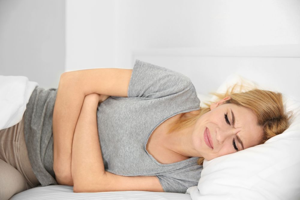 Person experiencing abdominal pain, lying in bed.